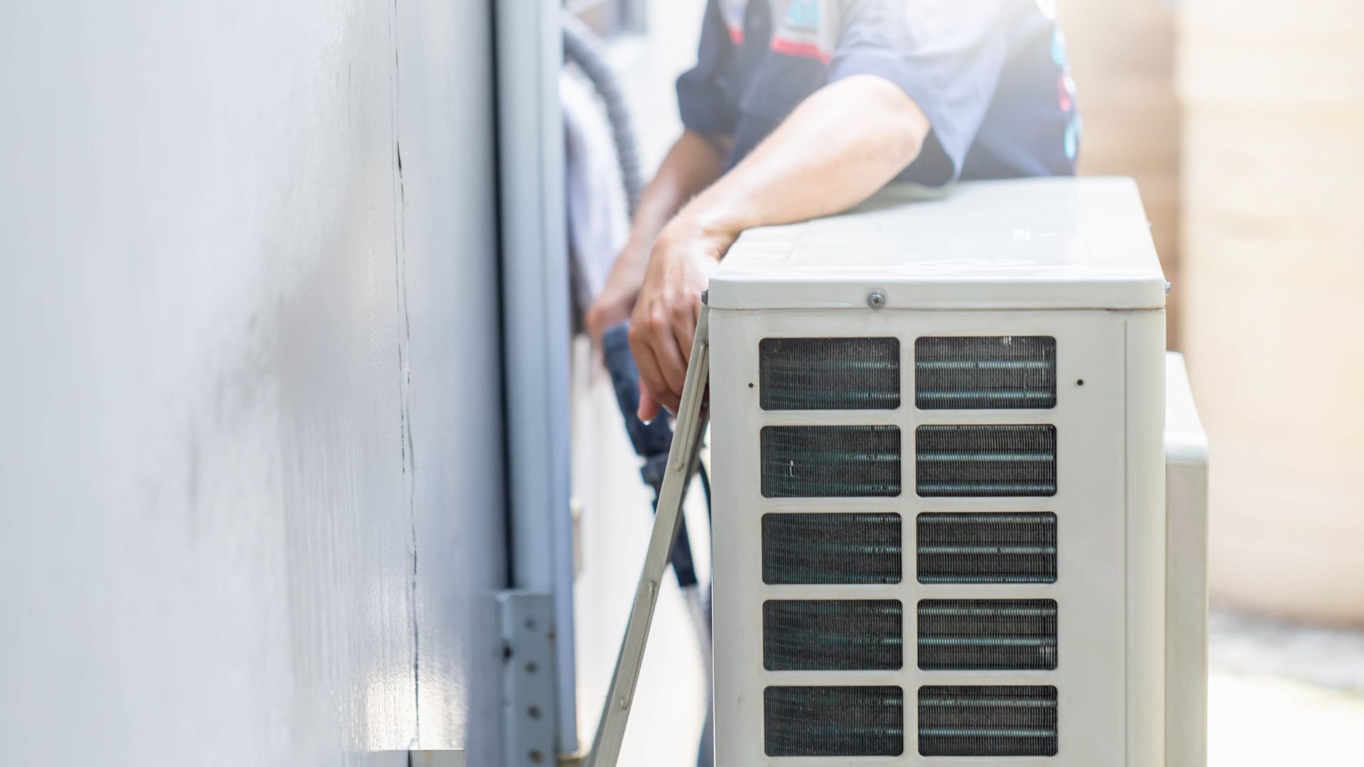 Technician working on an outdoor air conditioning unit with metal grid