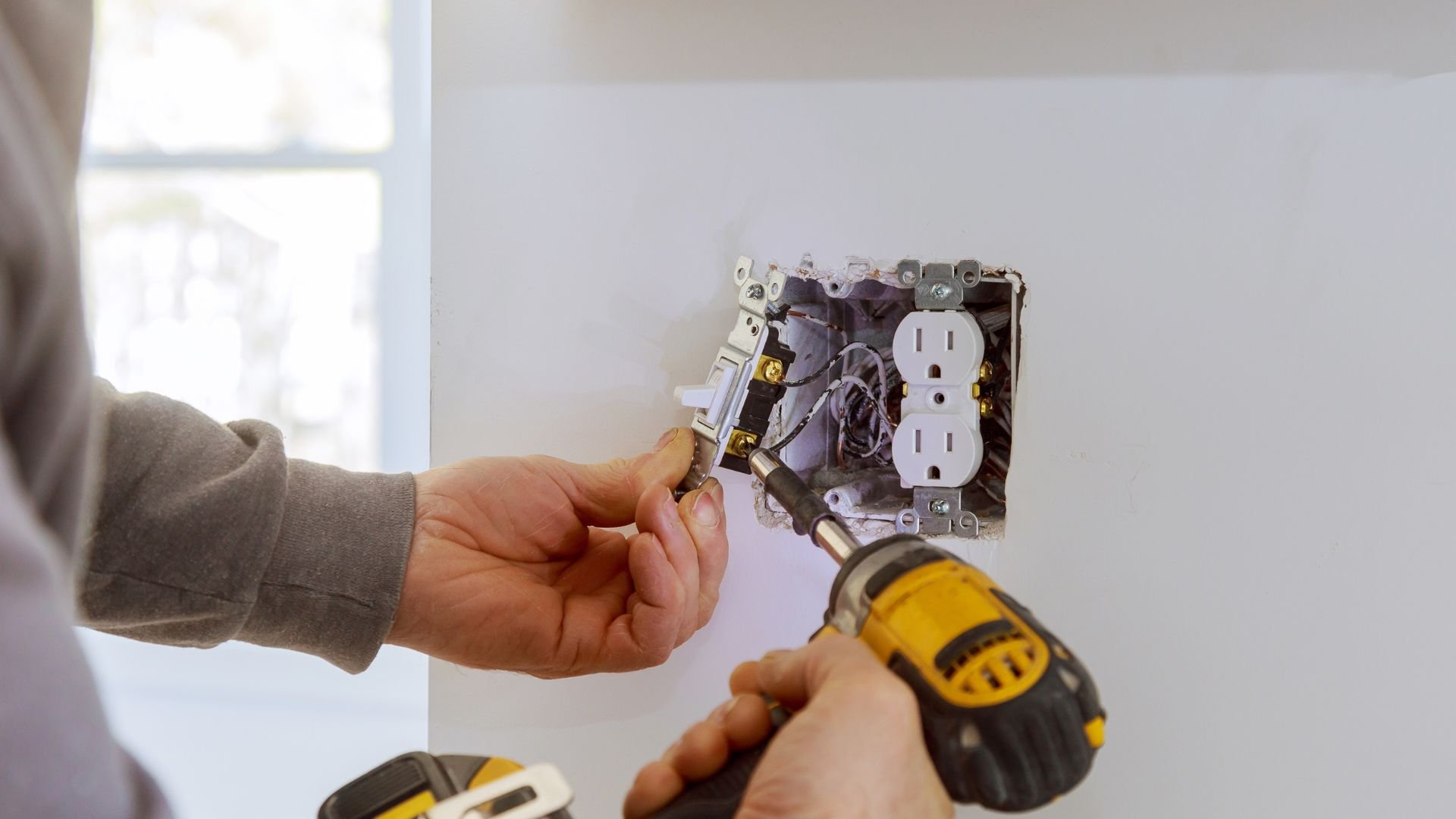 Electrician installing electrical outlet with power drill and wiring