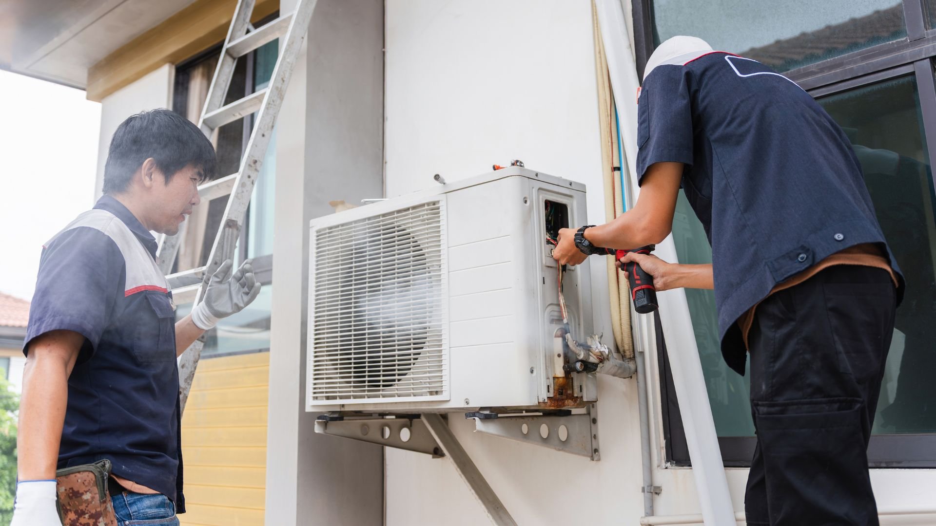 Technicians installing and repairing an air conditioning unit outside a building
