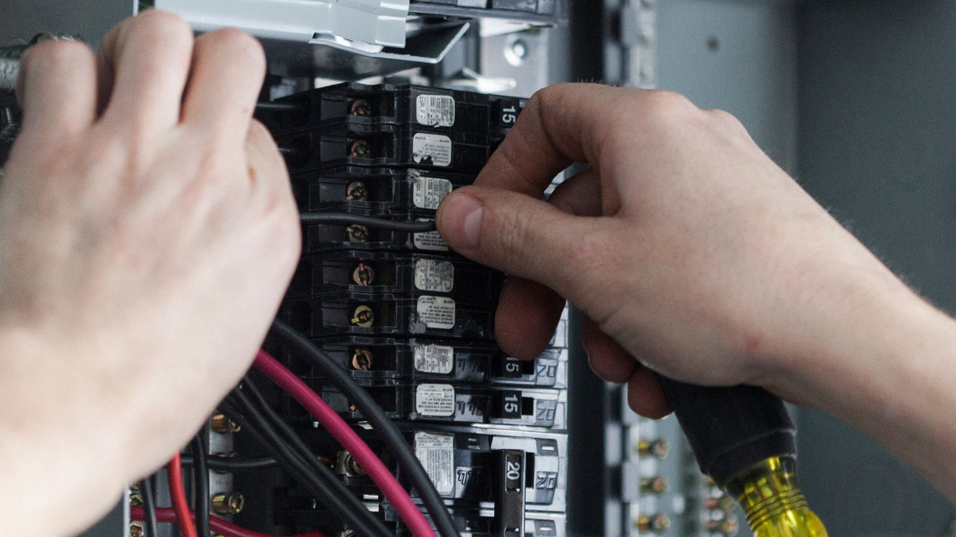 Hands checking electrical circuit breakers in an industrial electrical panel