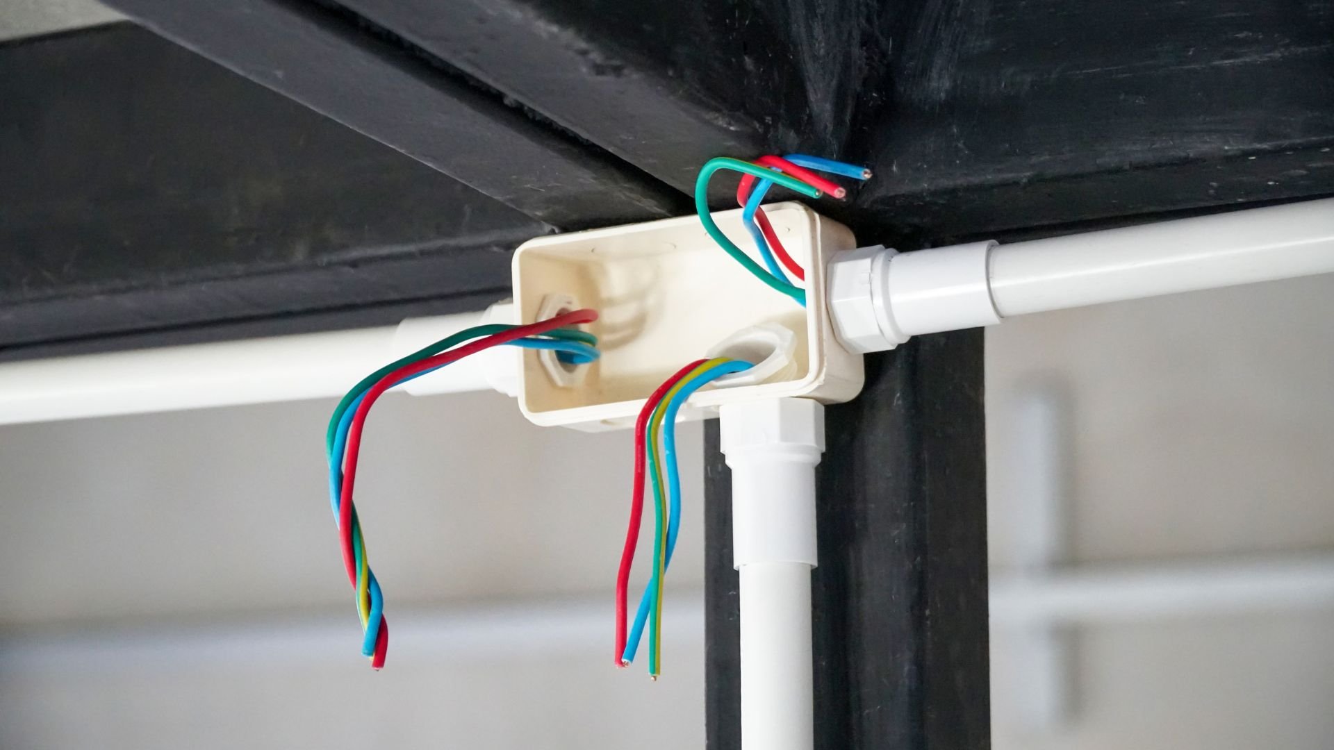 Exposed electrical wires connected to a white junction box and pipe