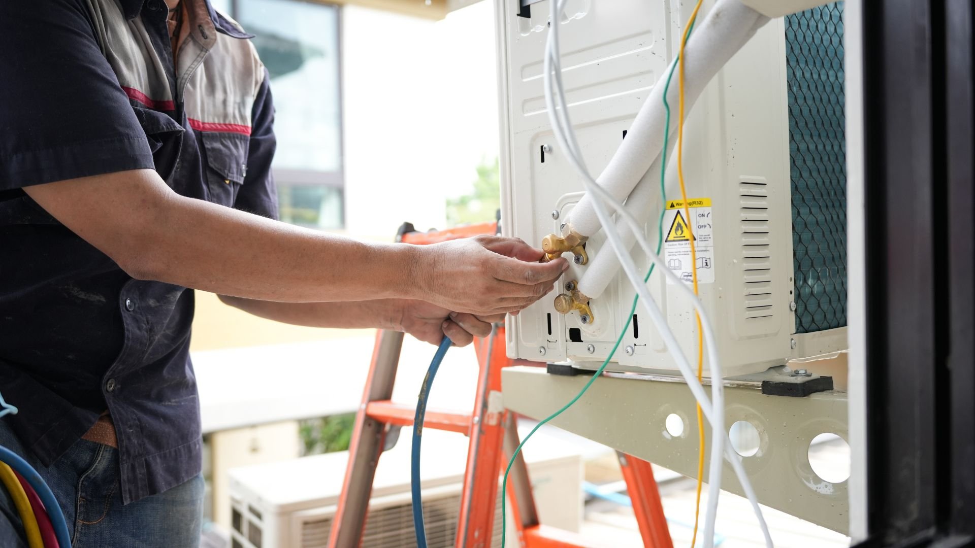 Technician working on electrical equipment with colored wires and orange ladder