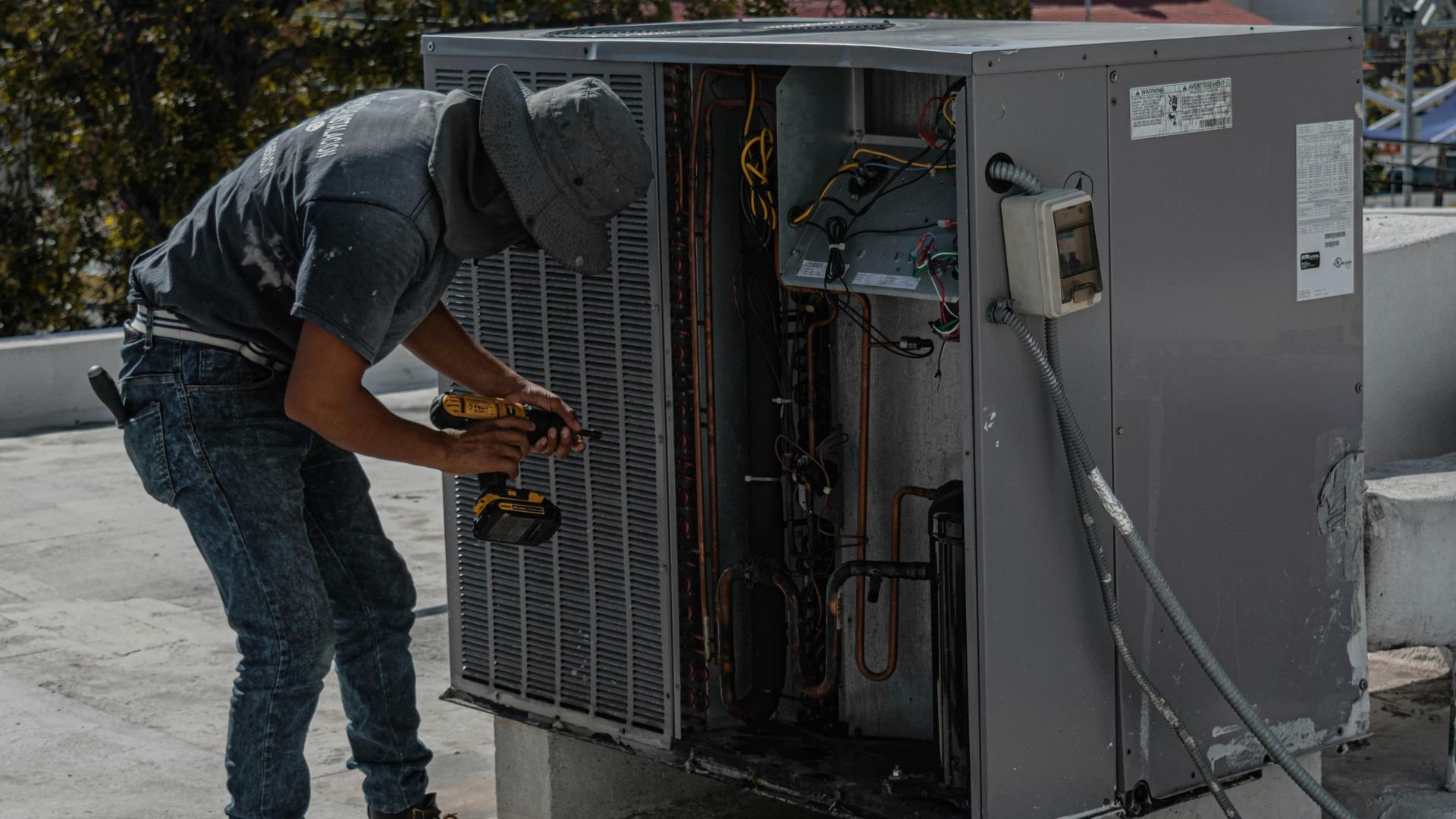 Technician repairing an air conditioning unit with a power drill