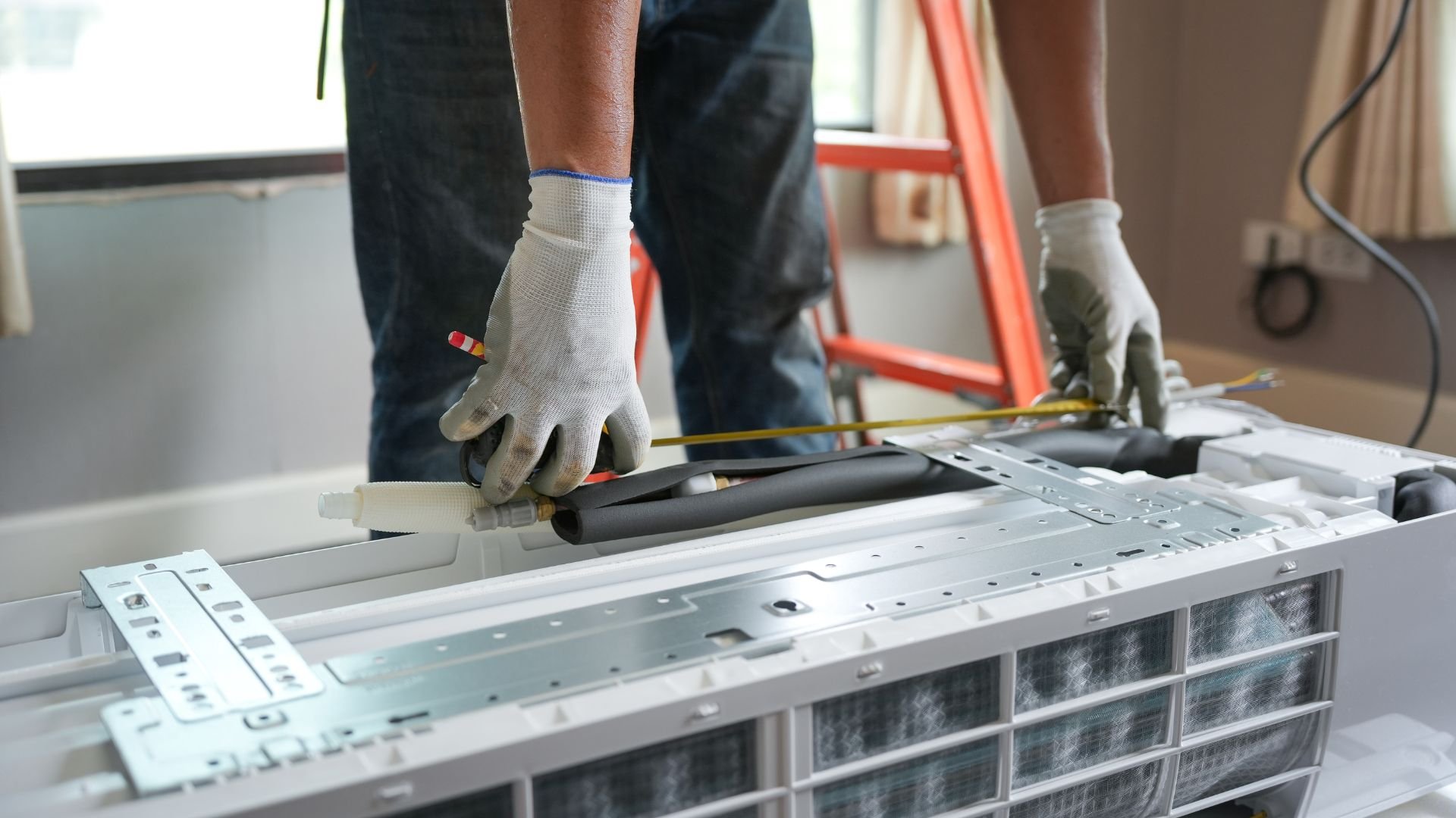 Worker installing air conditioning unit with gloved hands and measuring tape