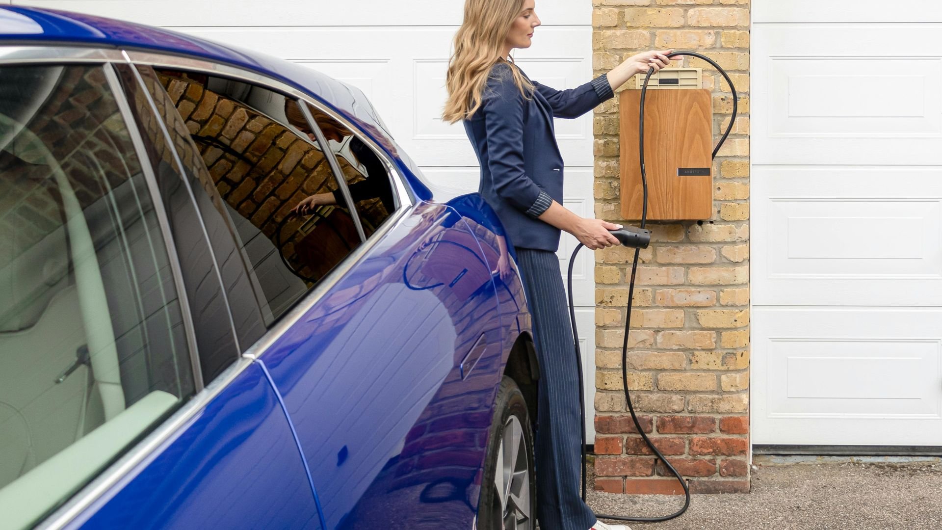 Woman charging blue electric vehicle at home wall charging station